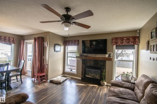 Living area featuring wood-finish flooring, a ceiling fan, and multiple windows providing natural light - 5121 52 Ave, St. Paul Town, AB - Indoor Photo Showing Living Room With Fireplace