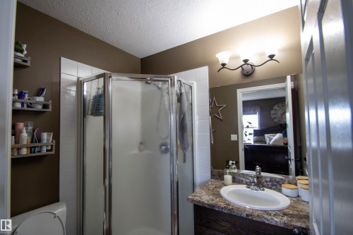 Compact bathroom featuring a corner shower with a chrome frame and frosted glass panels, a vanity with a laminate countertop and undermount sink, and a three-light fixture above the mirror - 5121 52 Ave, St. Paul Town, AB - Indoor Photo Showing Bathroom