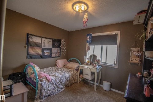 Carpeted room with a ceiling-mounted light fixture, a window featuring a roller blind, and neutral-toned wall paint - 5121 52 Ave, St. Paul Town, AB - Indoor Photo Showing Bedroom