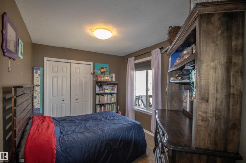 Bedroom featuring wood-finish flooring, a double-door closet with paneling, and a window with white drapes - 5121 52 Ave, St. Paul Town, AB - Indoor Photo Showing Bedroom
