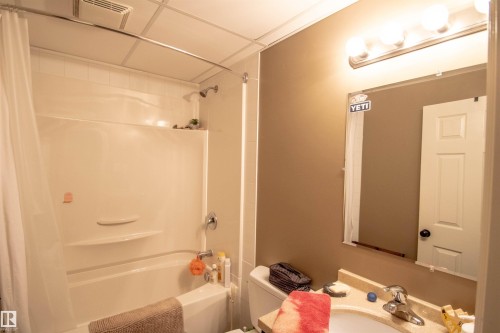 Bathroom featuring a white integrated shower/tub unit with chrome fixtures, a vanity with a light-toned countertop and integrated sink, a wall-mounted mirror, and a multi-bulb vanity light fixture - 5121 52 Ave, St. Paul Town, AB - Indoor Photo Showing Bathroom