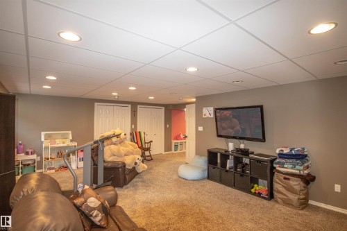 Carpeted living area featuring a drop-ceiling with recessed lighting, neutral wall tones, and white bi-fold closet doors - 5121 52 Ave, St. Paul Town, AB - Indoor