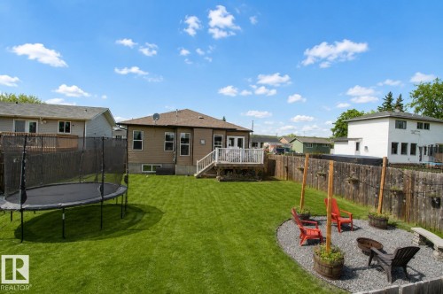 Expansive backyard featuring a manicured lawn, a gravel fire pit area with built-in seating, a privacy fence, and a rear deck with stairs - 5121 52 Ave, St. Paul Town, AB - Outdoor With Deck Patio Veranda