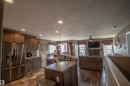 Open-concept living space featuring a kitchen with wood cabinetry and a stainless-steel refrigerator, a central island with a sink, wood-finish flooring, and a living area with a fireplace - 5121 52 Ave, St. Paul Town, AB  - Indoor Photo Showing Kitchen 
