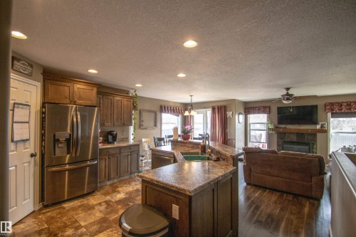 Open-concept kitchen featuring wood-finish flooring, recessed lighting, a stainless steel refrigerator, stone-look countertops, and an integrated kitchen island with a double basin sink - 5121 52 Ave, St. Paul Town, AB - Indoor Photo Showing Kitchen