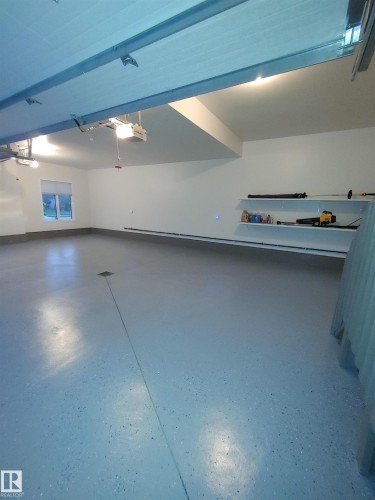 Spacious garage featuring an epoxy-coated floor, bright overhead lighting, and built-in wall shelving - 4125 Kennedy Green, Edmonton, AB - Indoor Photo Showing Other Room