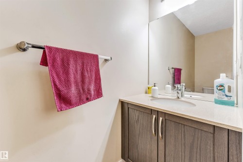 Bathroom featuring a wood-finish vanity with dual doors, a light-toned countertop, an integrated sink, and a wall-mounted mirror - 1715 27 Street, Edmonton, AB - Indoor Photo Showing Bathroom