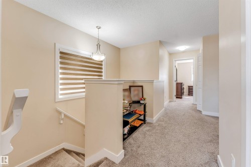Upper landing featuring light neutral wall paint, textured carpet flooring, white trim, a decorative pendant light fixture, and a window with horizontal blinds - 1715 27 Street, Edmonton, AB - Indoor Photo Showing Other Room