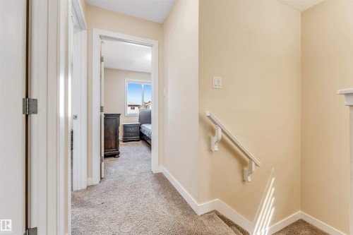 Carpeted hallway with a light beige wall color, white trim, and a white handrail leading to a carpeted staircase - 1715 27 Street, Edmonton, AB - Indoor Photo Showing Other Room