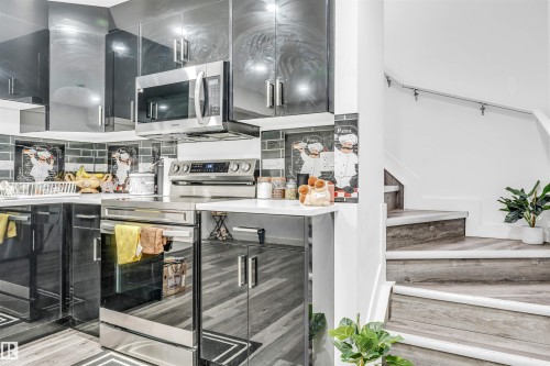 Modern kitchen featuring sleek black cabinetry with stainless steel hardware, stainless steel appliance suite, and light-tone countertops - 1715 27 Street, Edmonton, AB - Indoor