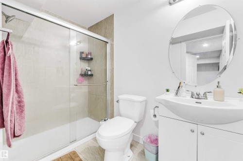 Bathroom featuring a walk-in shower with tile surround, a single vanity with a white countertop and basin, an oval mirror, and light-toned floor tiling - 1715 27 Street, Edmonton, AB - Indoor Photo Showing Bathroom