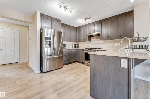 Modern kitchen featuring wood-finish flooring, dark wood cabinetry, a stainless steel refrigerator, and a stainless steel range with overhead vent - 1715 27 Street, Edmonton, AB - Indoor Photo Showing Kitchen With Upgraded Kitchen