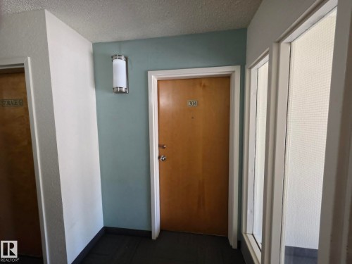 Entryway with a light wood-finish door and a cylindrical sconce light fixture, complemented by a textured ceiling - 304 34 Alpine Place, St. Albert, AB - Indoor Photo Showing Other Room