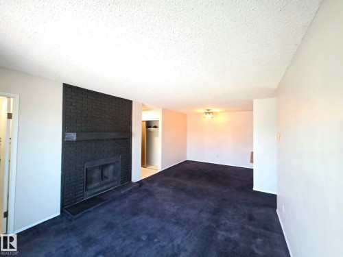 Living area featuring a black brick fireplace with a mantel, dark carpet flooring, and white walls - 304 34 Alpine Place, St. Albert, AB - Indoor With Fireplace