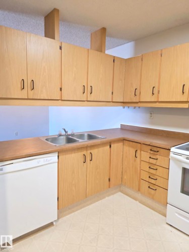 Kitchen featuring light wood-finish cabinetry with black hardware, laminate countertops, a stainless steel double basin sink, and a white dishwasher - 304 34 Alpine Place, St. Albert, AB - Indoor Photo Showing Kitchen With Double Sink
