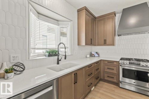 Modern kitchen featuring a bay window, white quartz countertops, light wood-finish cabinetry, a stainless steel gas range with coordinating vent hood, and a white tile backsplash - 7719 166 Avenue, Edmonton, AB - Indoor Photo Showing Kitchen With Double Sink With Upgraded Kitchen