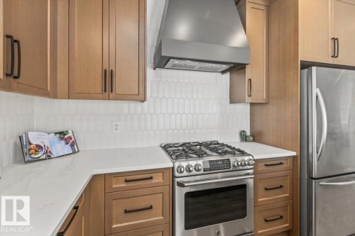 Modern kitchen featuring light wood cabinetry, a white picket tile backsplash, stainless steel appliances, and white countertops - 7719 166 Avenue, Edmonton, AB - Indoor Photo Showing Kitchen With Upgraded Kitchen