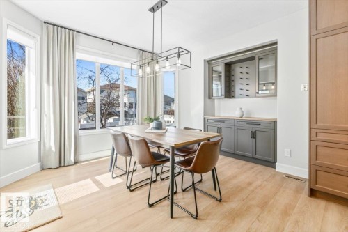 Dining area with wood-finish flooring, featuring a large window with white trim, and a recessed built-in cabinet system with gray lower cabinetry and open shelving - 7719 166 Avenue, Edmonton, AB - Indoor Photo Showing Dining Room