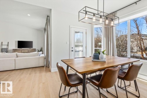 Dining area with a contemporary linear chandelier, large windows, and light wood-finish flooring - 7719 166 Avenue, Edmonton, AB - Indoor Photo Showing Dining Room