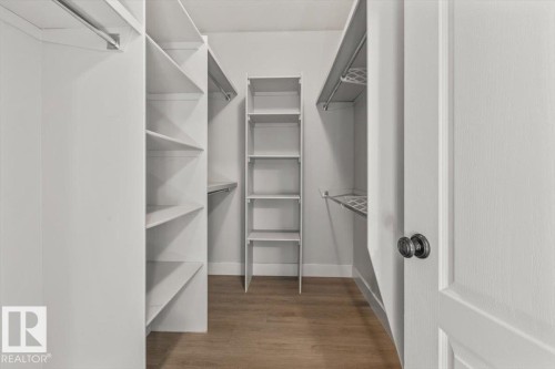 Walk-in closet featuring wood-finish flooring, white built-in shelving, white walls, and a white paneled door with dark hardware - 7719 166 Avenue, Edmonton, AB - Indoor With Storage