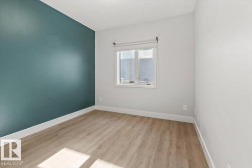 Room featuring a teal accent wall, wood-finish flooring, white baseboards, and a window with a roller shade - 7719 166 Avenue, Edmonton, AB - Indoor Photo Showing Other Room