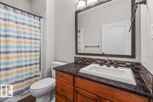 Bathroom featuring a dark wood vanity with a dark countertop, an undermount sink, and a tiled backsplash - 7719 166 Avenue, Edmonton, AB - Indoor Photo Showing Bathroom