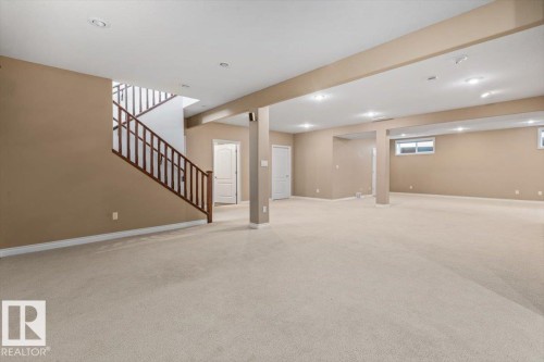 Expansive carpeted area featuring recessed lighting, a wood staircase with white risers, and neutral-toned walls - 7719 166 Avenue, Edmonton, AB - Indoor