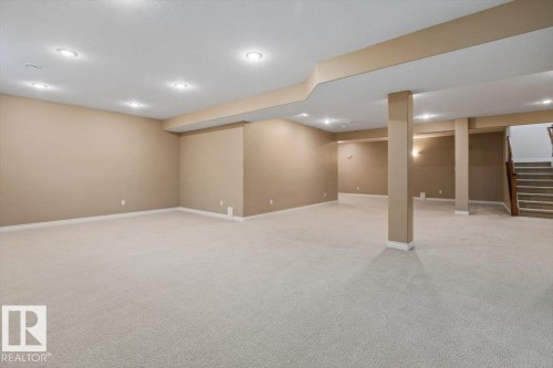 Spacious carpeted room featuring recessed lighting, neutral-toned walls, and a staircase with wood-finish handrails - 7719 166 Avenue, Edmonton, AB - Indoor Photo Showing Basement