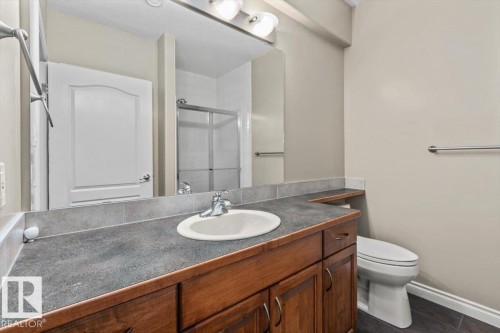 Bathroom featuring a single vanity with wood-finish cabinetry, a dark countertop, a ceramic sink, a mirror, and a toilet - 7719 166 Avenue, Edmonton, AB - Indoor Photo Showing Bathroom