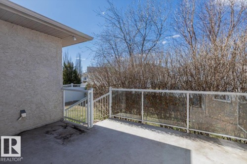 Concrete patio featuring stucco siding, glass panel railing, and white metal handrails - 7719 166 Avenue, Edmonton, AB - Outdoor