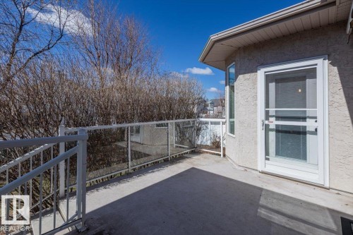 Exterior deck featuring a concrete surface, white metal railing with glass panels, and an exterior door with a screen - 7719 166 Avenue, Edmonton, AB - Outdoor