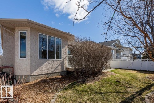 Rear exterior featuring a stucco finish, large bay window, vertical window, and a white privacy fence - 7719 166 Avenue, Edmonton, AB - Outdoor