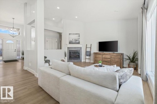 Open-concept living area featuring light wood-finish flooring, recessed lighting, and a contemporary fireplace with a stone surround - 7719 166 Avenue, Edmonton, AB - Indoor Photo Showing Living Room With Fireplace
