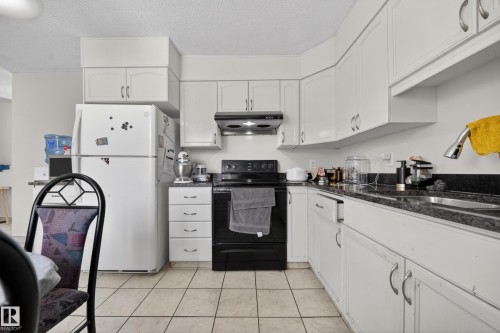 Kitchen featuring white cabinetry with silver hardware, dark granite-style countertops, stainless steel sink, and a black range with an overhead exhaust fan - 8312 29 Ave Nw, Edmonton, AB - Indoor Photo Showing Kitchen