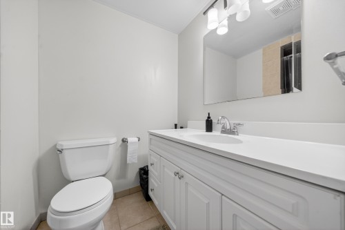 Bathroom featuring a white vanity with paneling, a white countertop, chrome fixtures, an integrated sink, and a rectangular mirror - 8312 29 Ave Nw, Edmonton, AB - Indoor Photo Showing Bathroom