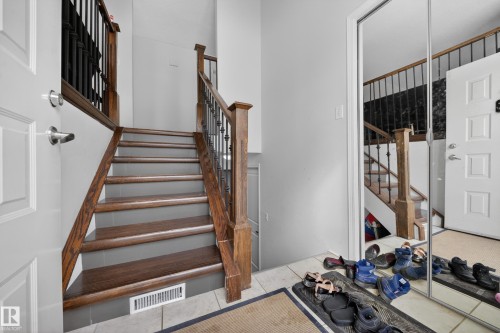 Foyer featuring a hardwood staircase with dark metal balusters, light gray wall paint, tiled flooring, and a mirrored sliding closet door - 8312 29 Ave Nw, Edmonton, AB - Indoor Photo Showing Other Room