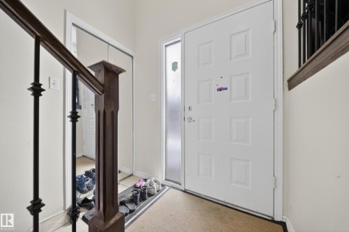 Entryway featuring a paneled door with frosted glass sidelight, wood-finish staircase railing with black metal spindles, and a mirrored closet door - 8312 29 Ave Nw, Edmonton, AB - Indoor Photo Showing Other Room