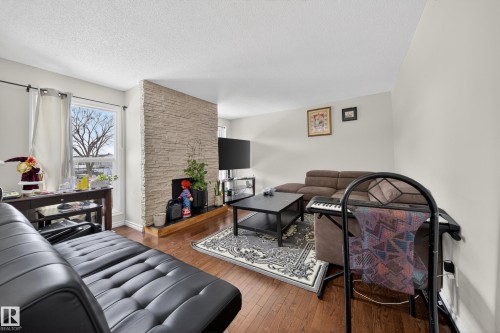 Spacious living area featuring wood-finish flooring, light-colored walls, and a stone-faced fireplace with a black hearth - 8312 29 Ave Nw, Edmonton, AB - Indoor Photo Showing Living Room