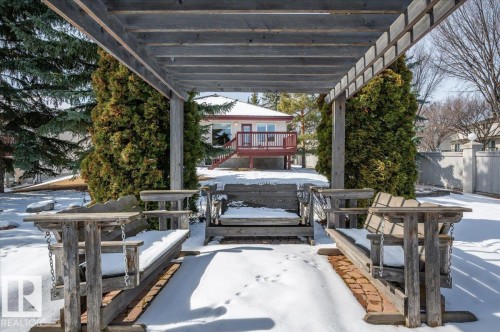 The property features a pergola with wooden swing benches, set on a brick pathway, surrounded by mature trees. The bungalow can be seen in the distance. - 19 1203 Carter Crest Road, Edmonton, AB - Outdoor With Deck Patio Veranda