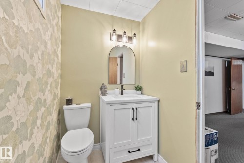 Bathroom featuring a white vanity with cabinet and drawer storage, black hardware, an arched mirror, and a three-light fixture - 13516 104A Street, Edmonton, AB - Indoor Photo Showing Bathroom