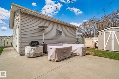 Concrete patio area featuring string lighting, a wooden privacy fence, a detached shed, and a section of green lawn - 13516 104A Street, Edmonton, AB - Outdoor With Exterior