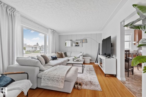 Spacious living area featuring large picture windows, wood-finish flooring, and a decorative accent wall - 13516 104A Street, Edmonton, AB - Indoor Photo Showing Living Room