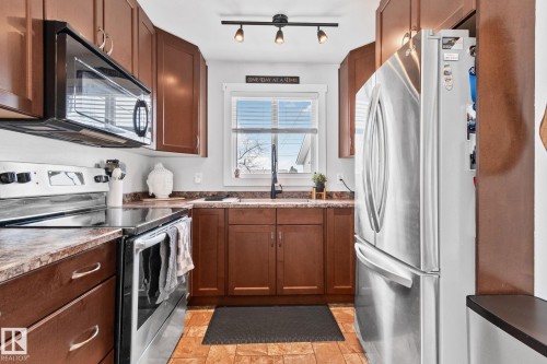 Kitchen featuring wood-finish cabinetry, stainless steel appliances, and a window above the sink - 13516 104A Street, Edmonton, AB - Indoor Photo Showing Kitchen