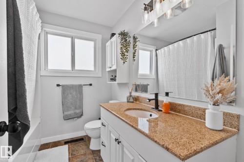 Bathroom featuring a white vanity with panel cabinetry and black hardware, a light brown stone-finish countertop, and a black single-handle faucet - 13516 104A Street, Edmonton, AB - Indoor Photo Showing Bathroom