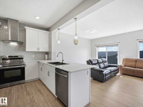 Open-concept kitchen featuring white cabinetry, stainless steel appliances, a subway tile backsplash, and light wood-finish flooring - 2435 12 Avenue, Edmonton, AB - Indoor Photo Showing Kitchen With Double Sink