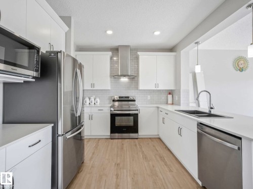 Modern kitchen featuring white cabinetry, stainless steel appliances, light wood-finish flooring, a subway tile backsplash, and a double basin sink - 2435 12 Avenue, Edmonton, AB - Indoor Photo Showing Kitchen With Stainless Steel Kitchen With Double Sink With Upgraded Kitchen