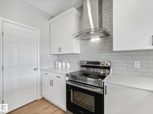 Kitchen featuring white shaker-style cabinetry, a stainless steel range with a matching vent hood, light-toned countertops, subway tile backsplash, and wood-finish flooring - 2435 12 Avenue, Edmonton, AB - Indoor Photo Showing Kitchen