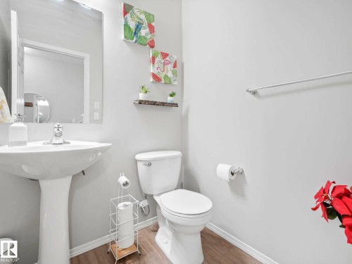 Pedestal sink with chrome faucet, wall-mounted mirror, white toilet, and wood-finish flooring - 2435 12 Avenue, Edmonton, AB - Indoor Photo Showing Bathroom