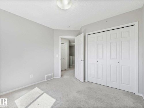 Carpeted room featuring light-toned walls, white trim, a flush-mount ceiling light fixture, and two sets of bi-fold closet doors with round silver-toned knobs - 2435 12 Avenue, Edmonton, AB - Indoor