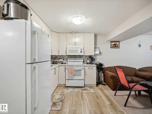 Kitchen area featuring light wood-finish flooring, white cabinetry, and a white appliance suite including a refrigerator, stove, and microwave - 2435 12 Avenue, Edmonton, AB - Indoor Photo Showing Kitchen